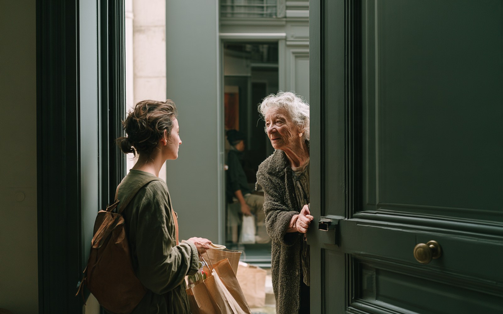 Une voisine apporte des courses à une habitante sur le pas de sa porte, entraide de proximité